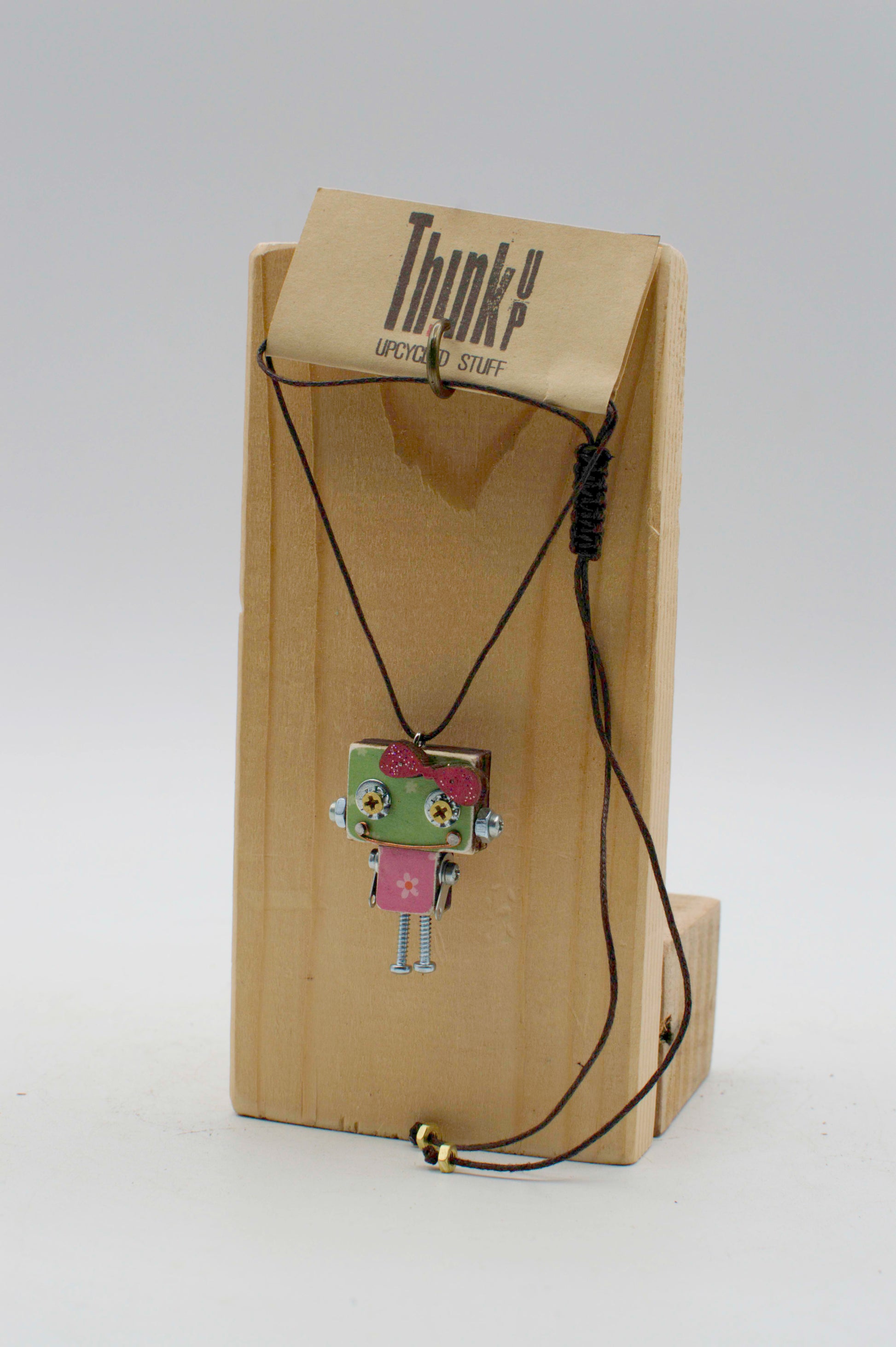Ciondolino robot in legno tagliato a laser verde e rosa con dettagli metallici esposto su supporto di legno