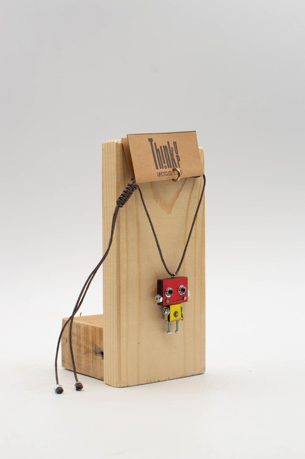 Ciondolino robot in legno tagliato a laser con pendente rosso e giallo e cordoncino intrecciato marrone su supporto in legno