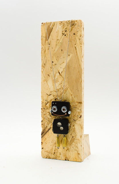 Ciondolo robot in legno nero con occhi argentati e gambe pendenti color oro su base in legno