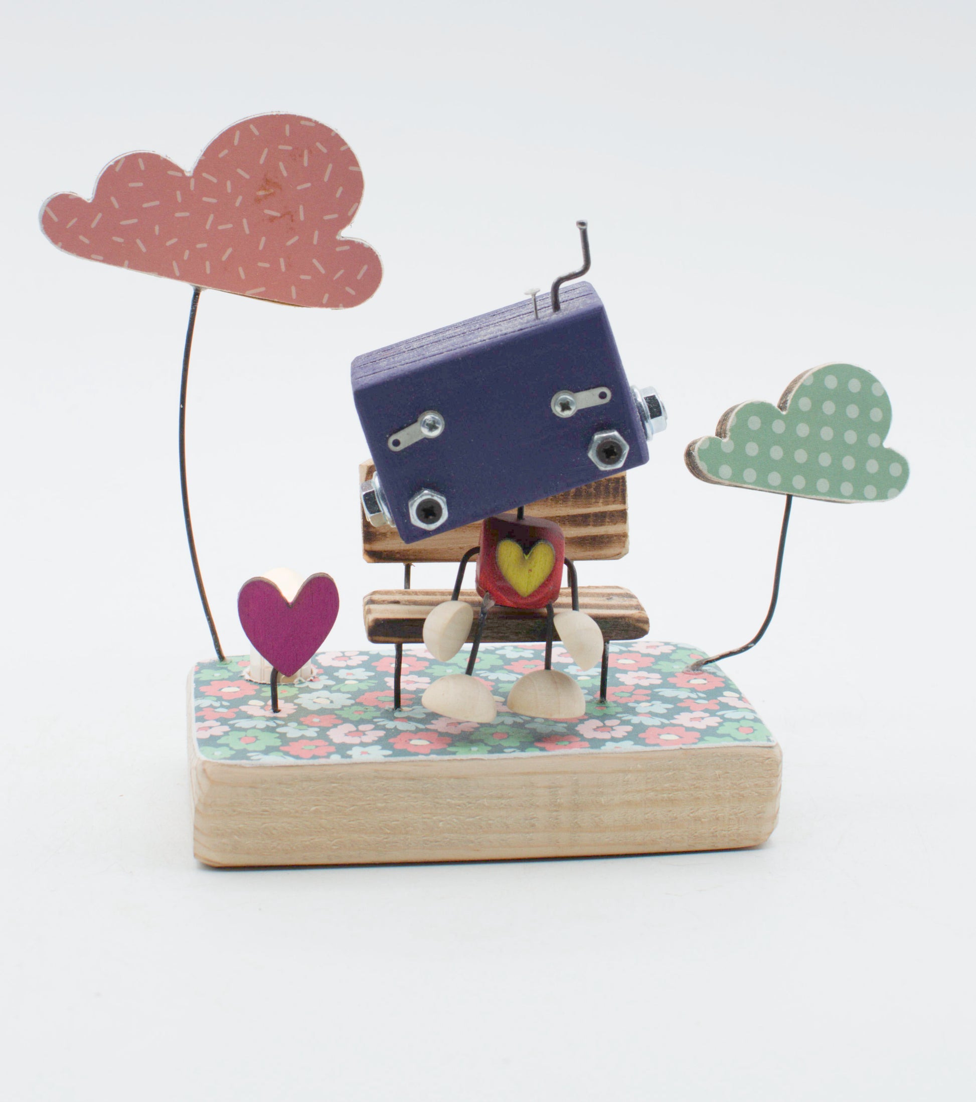 Diorama scultura luminosa stile robot fatto a mano in legno blu navy con occhi e giunture metallici seduto su panca floreale