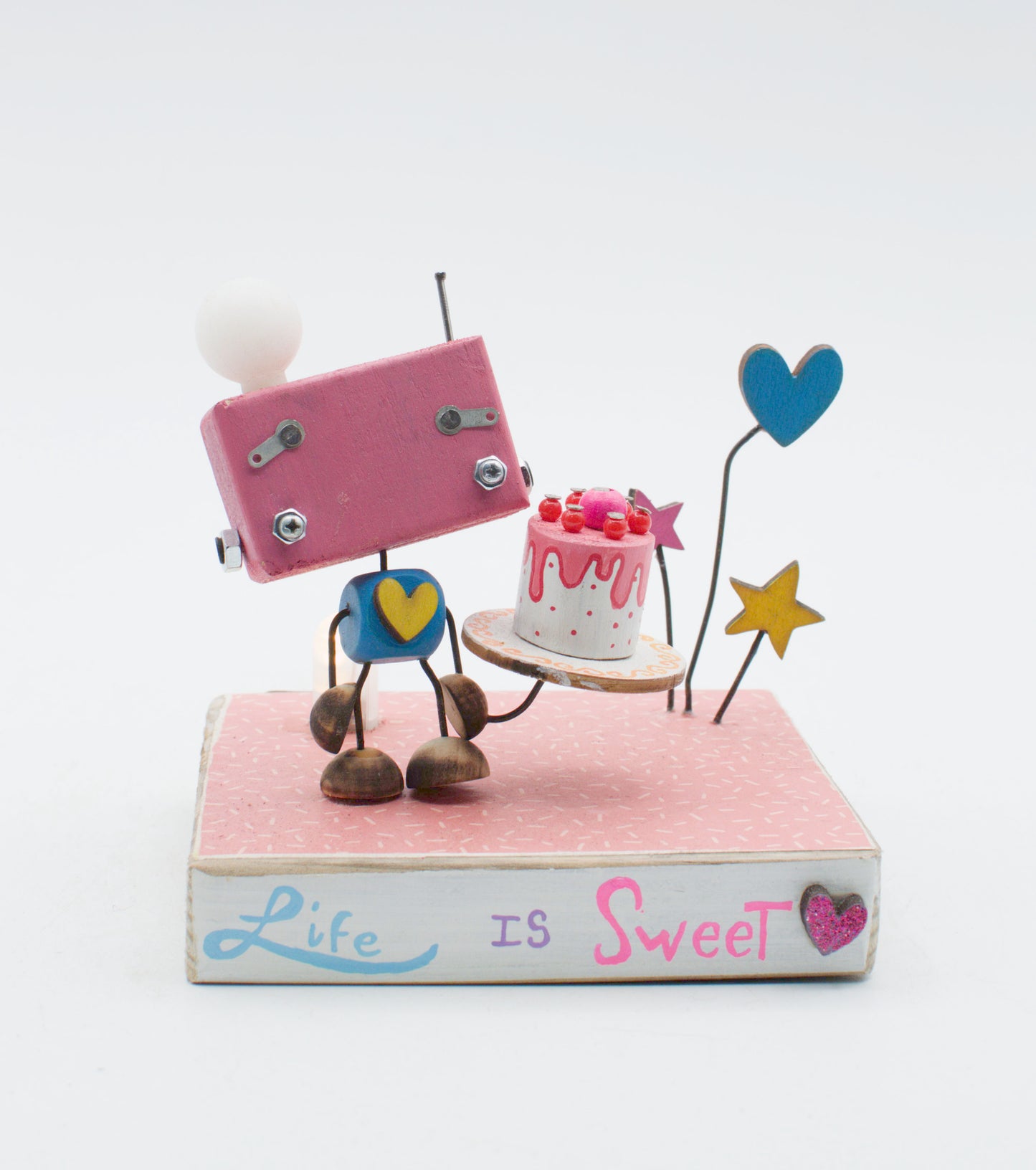 Diorama scultura luminosa stile robot fatto a mano rosa con testa bianca e cuore giallo che tiene torta su vassoio in legno