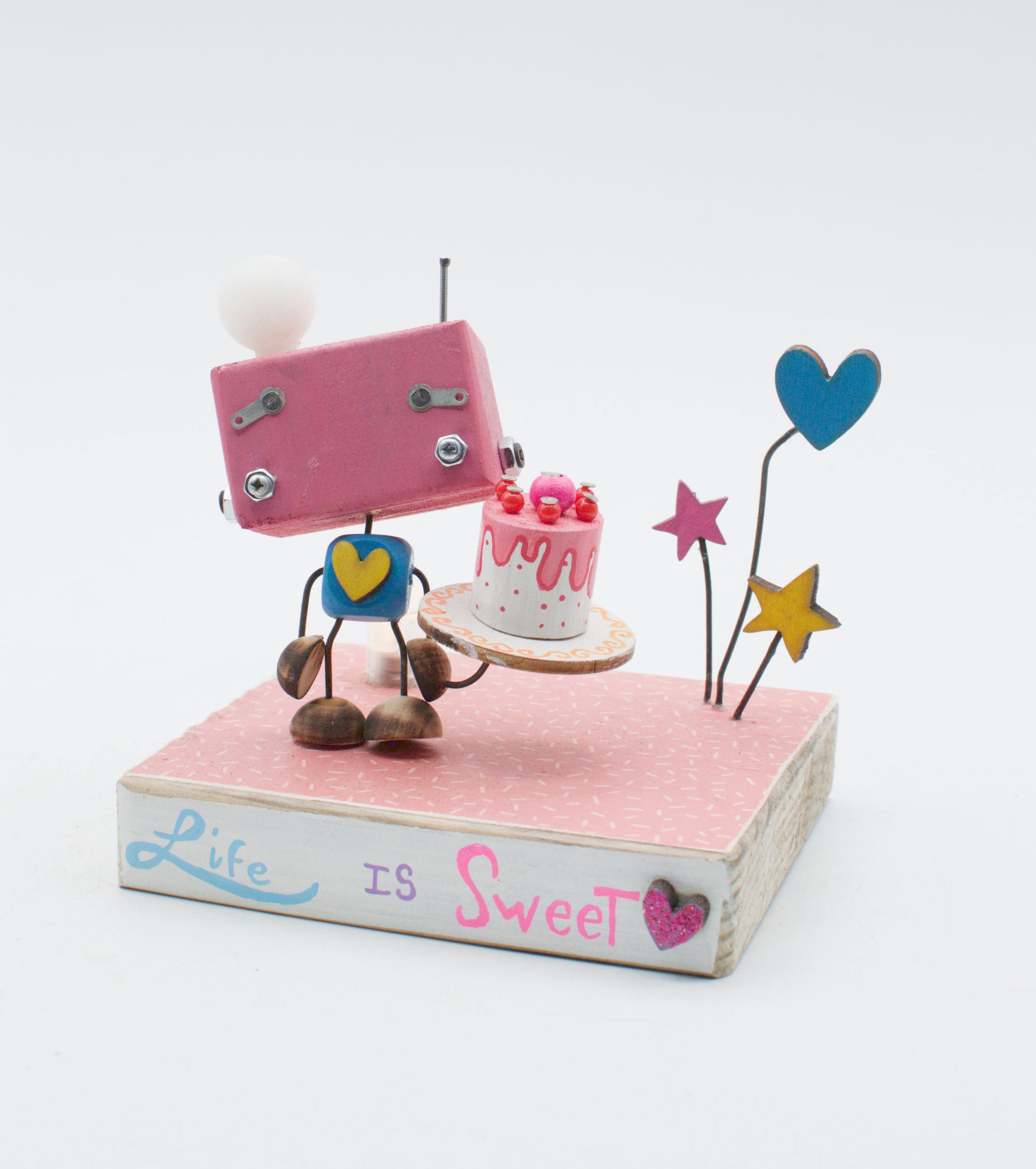 Diorama scultura luminosa robot rettangolare rosa con testa sfera bianca cuore blu e torta miniatura rosa su base legno