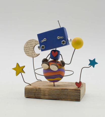 Diorama scultura luminosa robot in legno blu con corpo sferico arancione e viola, tiene una luna e una palla gialla di carta