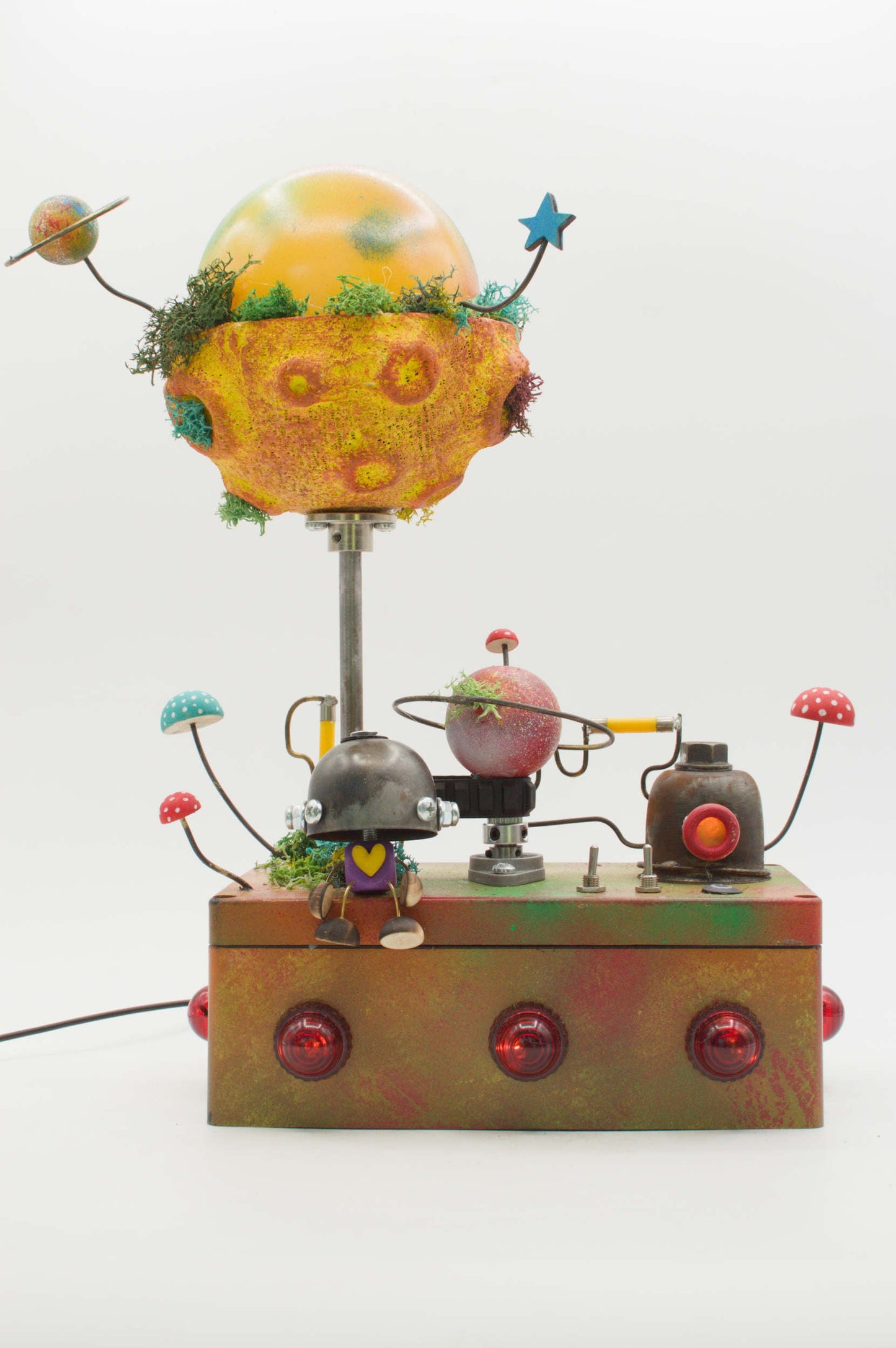 Lampada robot artigianale in metallo riciclato con pianeta giallo arancione e muschio verde su base metallica