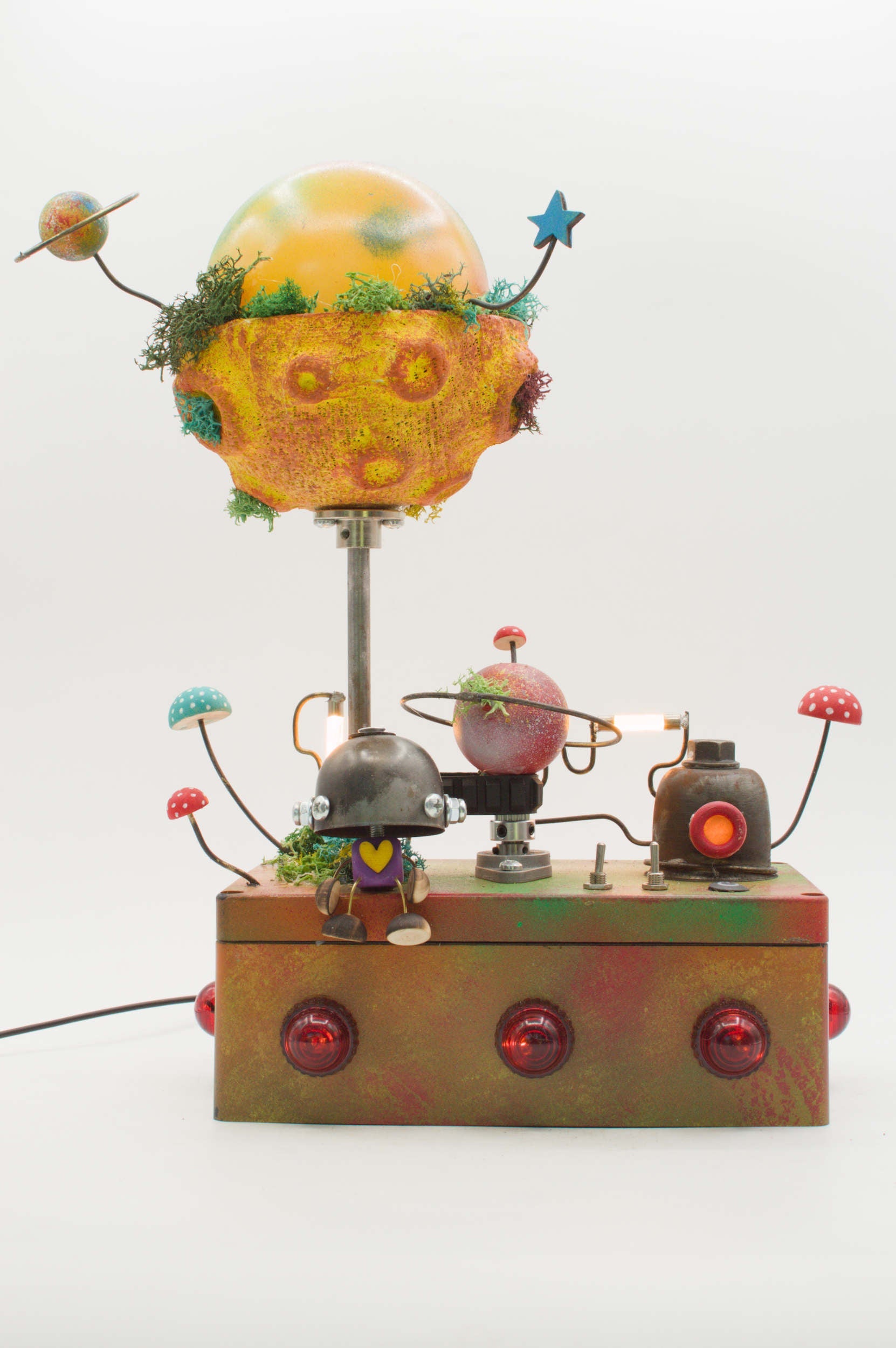 Lampada robot artigianale metallo riciclato con pianeta giallo arancio, muschio verde e figure robotiche in stile fantascientifico