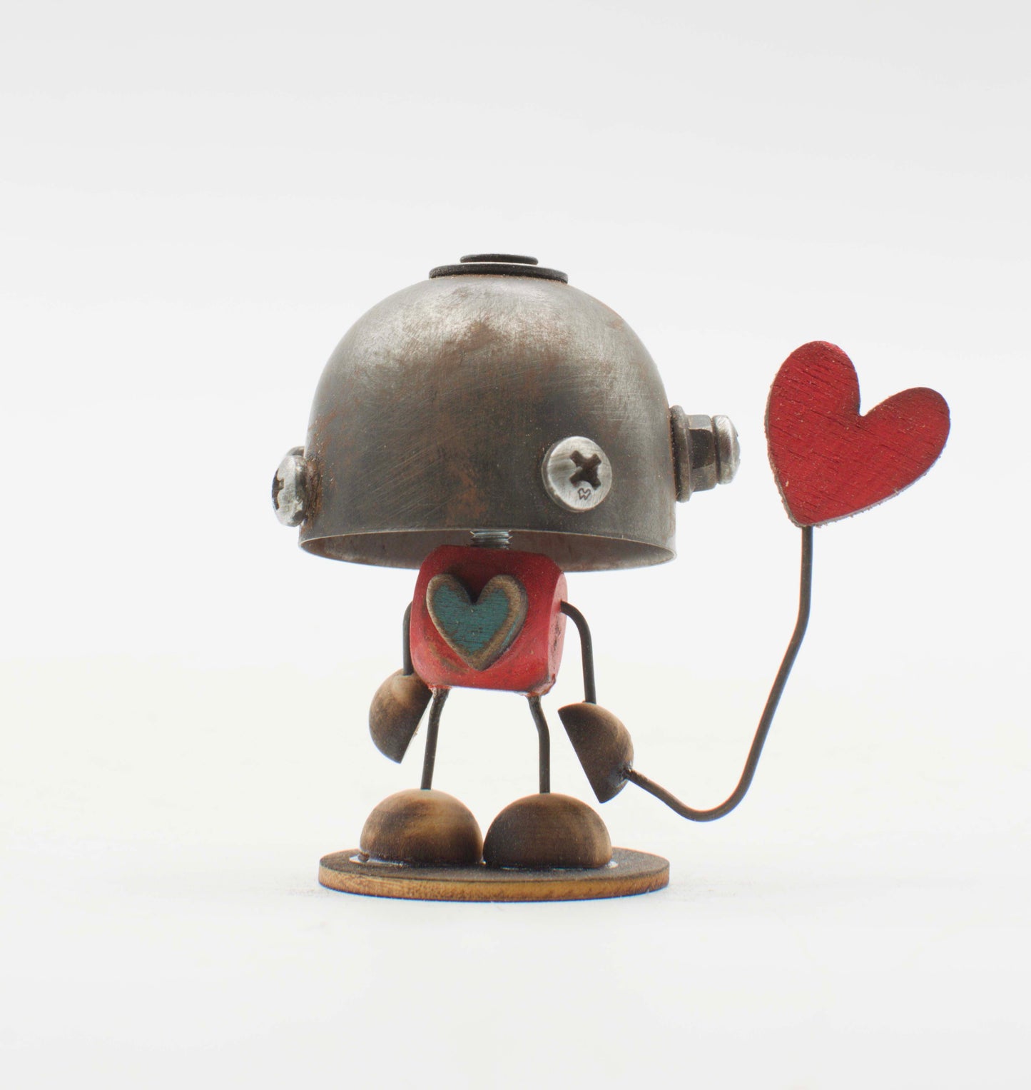Minibot scultura robot fatto a mano con testa in metallo argentato arrugginito, torso rosso con cuore turchese e piedi in legno tiene cuore rosso