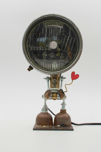 Robot lampada da tavolo stile fanale con testa circolare nera e cuore rosso su braccio metallico riciclato