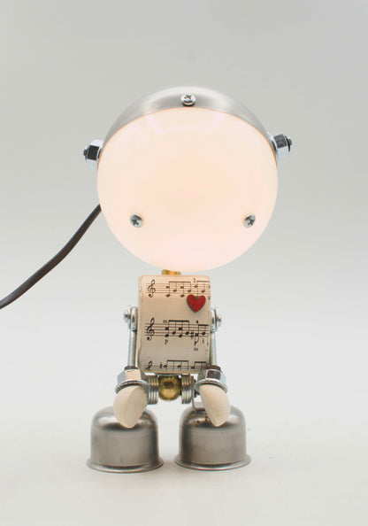 Lampada da tavolo robot kodama fatta a mano in metallo con testa luminosa circolare e corpo di spartiti musicali con cuore rosso